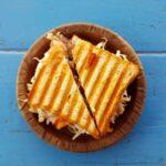 a perfectly golden sandwich made on a sandwich maker resting on a plate seen from above on top of a blue table