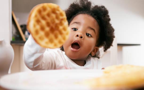 A happy and excited toddler holding a round waffle