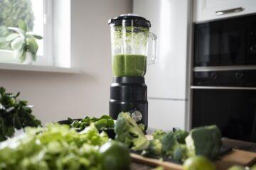 Blender in a kitchen worktop with green juice inside and the green juice ingredients around it.