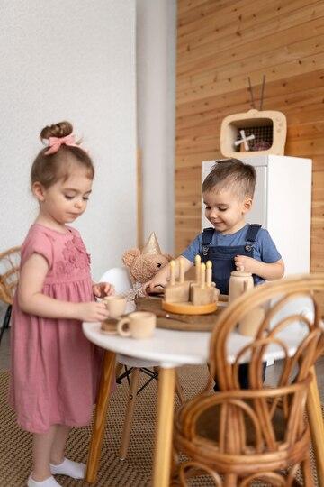 little girl and a toddler playing pretend tea party with wooden cake toy and wooden teacups and their teddy bear