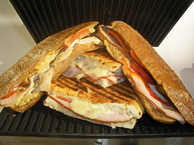 four slices of perfectly golden toasties resting on the sandwich maker, you can see a little bit of the filling inside - melted cheese, ham and tomato