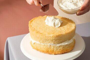 A round sponge cake with a bakers putting cream with a spatula