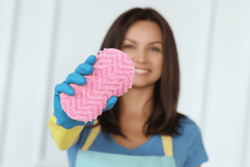 Woman holding a sponge for the camera, she is wearing blue rubber gloves