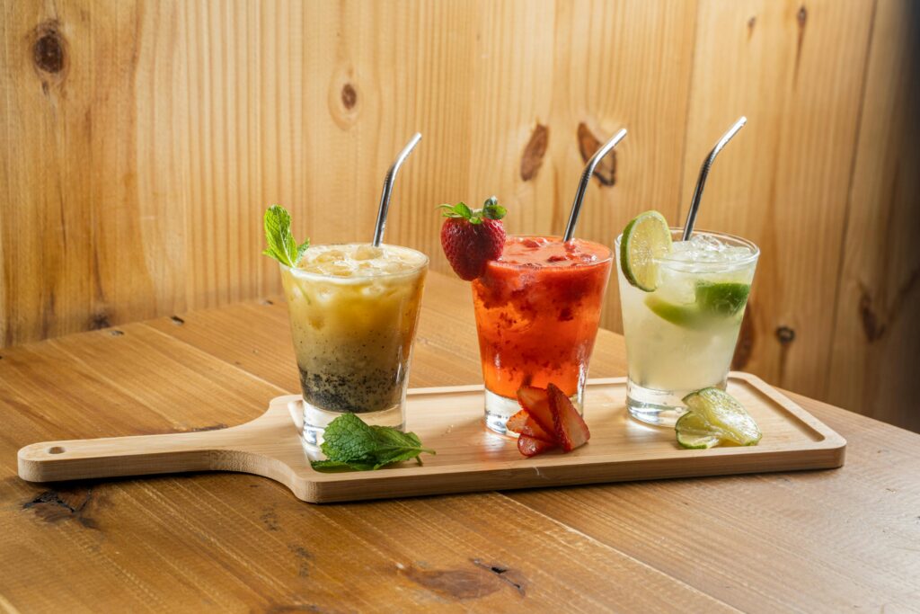 Three colorful cocktails with fruits on a wooden board, perfect for summer refreshment.