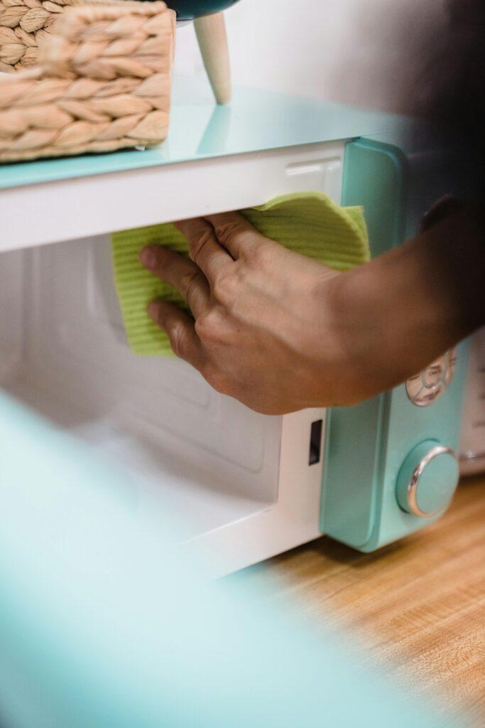 Close-up of hand cleaning a microwave with a cloth, focusing on household chores.
