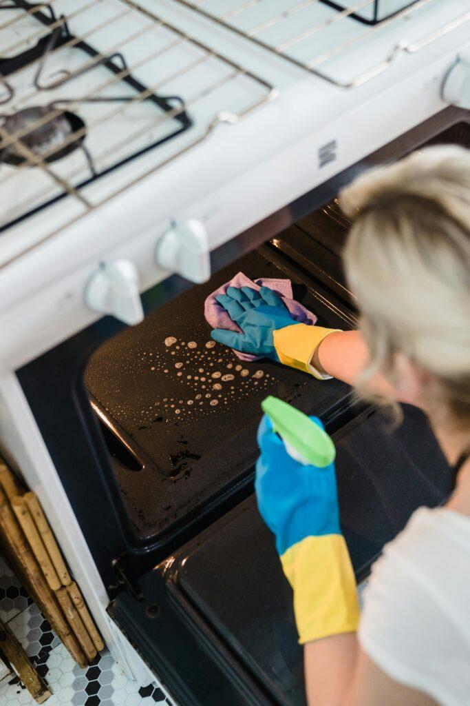 A woman wearing gloves cleans an oven in a domestic kitchen setting.