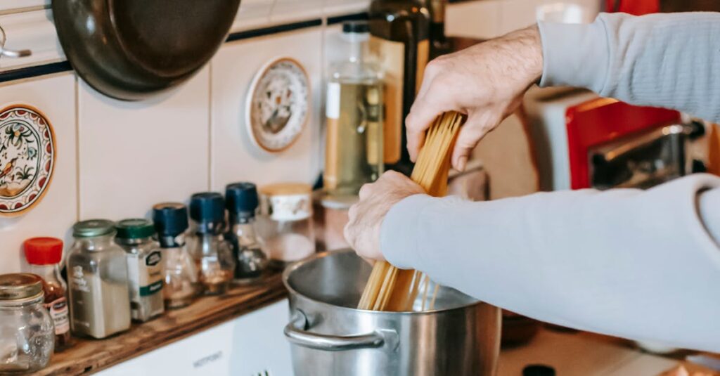A cozy kitchen scene with someone cooking pasta and sauce on a stove, surrounded by cookware.